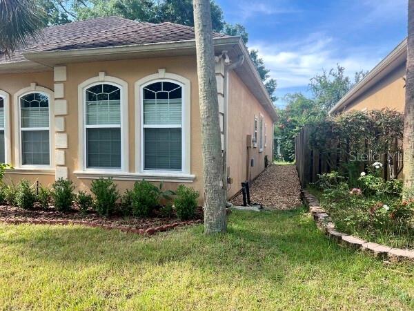 The exterior side of a tan stucco house features arched windows and a gravel path — 8913 SW 74TH AVENUE, GAINESVILLE, FL