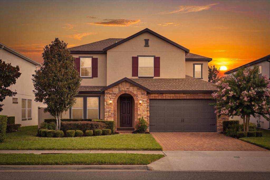 A two-story suburban house with a stone-accented entryway, a two-car garage, and a sunset sky — 16971 TRADEWIND POINT, WINTER GARDEN, FL