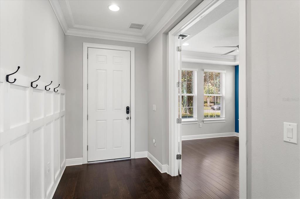 An entryway with dark wood floors, white wainscoting, coat hooks, and a view into another room — 16971 TRADEWIND POINT, WINTER GARDEN, FL