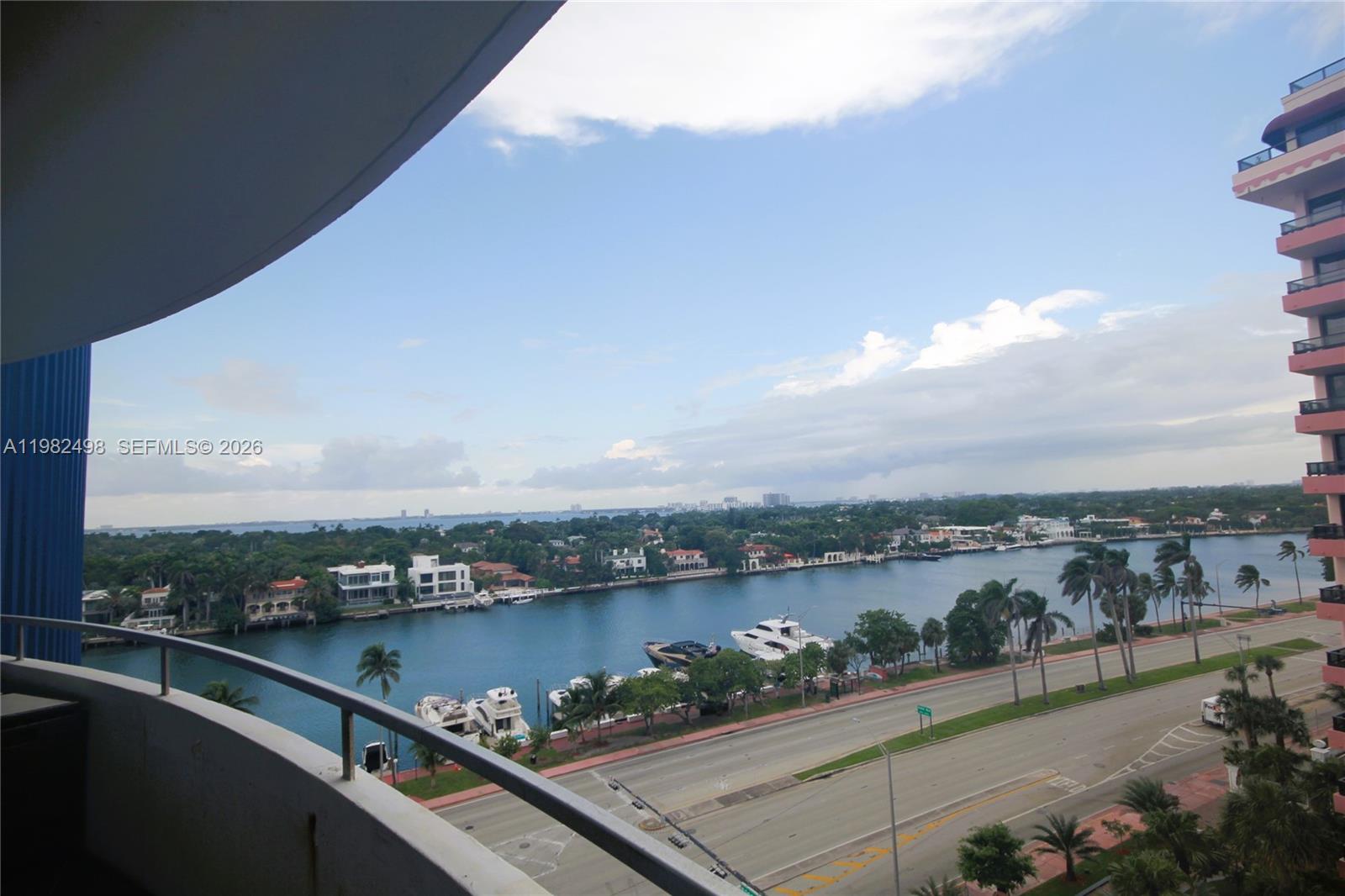 A balcony view overlooks a waterway, a coastal road, and a high-rise building — 5161 COLLINS AV # 1004, Miami Beach FL 33140, MIAMI BEACH, FL