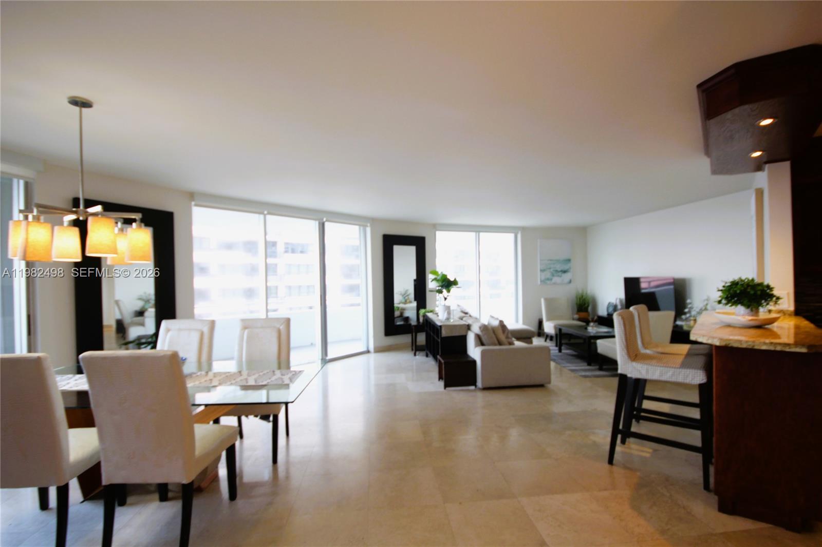 An open-concept living and dining area features tile flooring, floor-to-ceiling windows, and a breakfast bar — 5161 COLLINS AV # 1004, Miami Beach FL 33140, MIAMI BEACH, FL