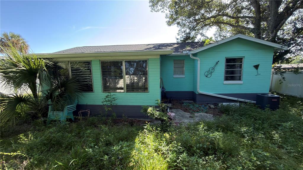 The exterior of a light green, single-story house with a dark gray base and overgrown yard — 856 BERKSHIRE ROAD, DAYTONA BEACH, FL