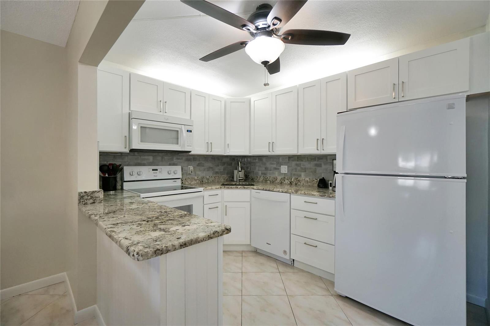 A kitchen features white cabinets, granite countertops, a tile backsplash, and a ceiling fan — 444 Pine Glen Lane # 1, FL 33463, FL