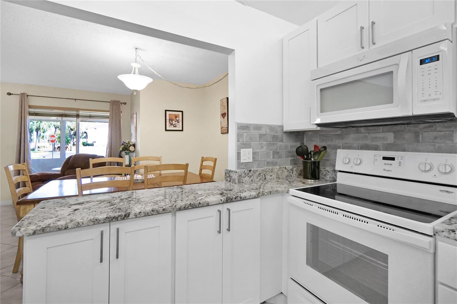 A kitchen with white cabinets, granite countertops, and a subway tile backsplash overlooks a dining area — 444 Pine Glen Lane # 1, FL 33463, FL