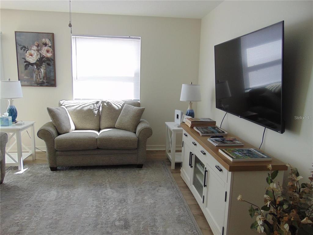 A living room features a loveseat, a television mounted above a media console, and rugs — 1420 FAIRWAY STREET, THE VILLAGES, FL