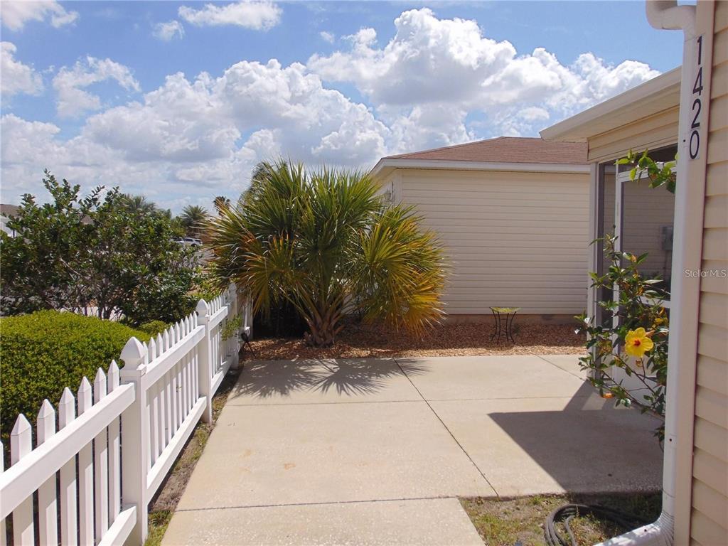 A concrete patio sits beside a house with a white fence and a palm tree — 1420 FAIRWAY STREET, THE VILLAGES, FL