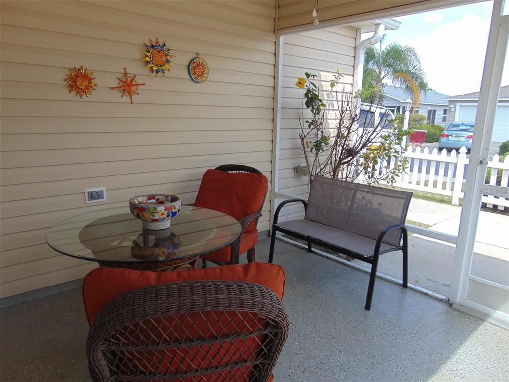 A screened-in porch features a glass-topped table, wicker chairs, a metal bench, and wall decor — 1420 FAIRWAY STREET, THE VILLAGES, FL