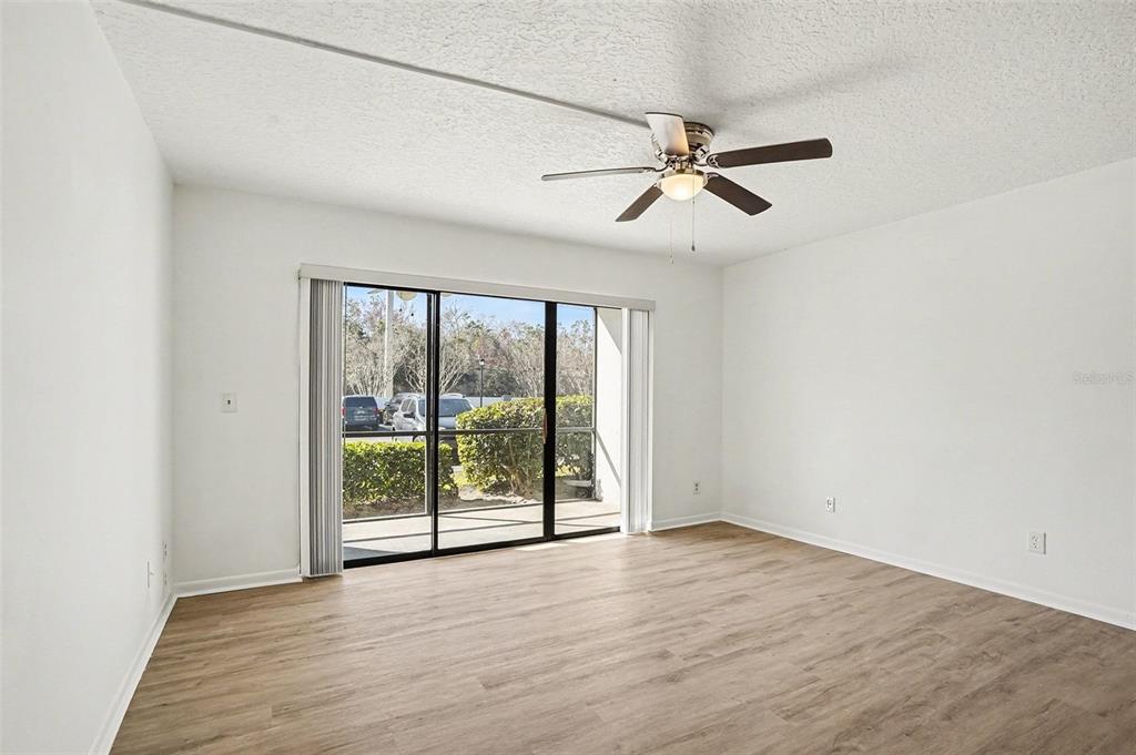 A bright, empty room features light wood-look flooring, a ceiling fan, and sliding glass doors — 1013 S PINE RIDGE CIRCLE UNIT 3C, SANFORD, FL
