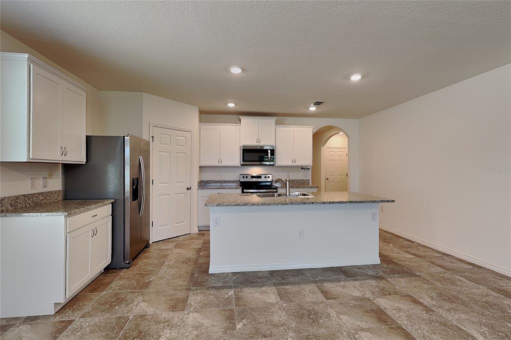 A kitchen with white cabinets, granite countertops, a stainless steel refrigerator, and tiled flooring — 3641 PEONY COURT SE, PALM BAY, FL