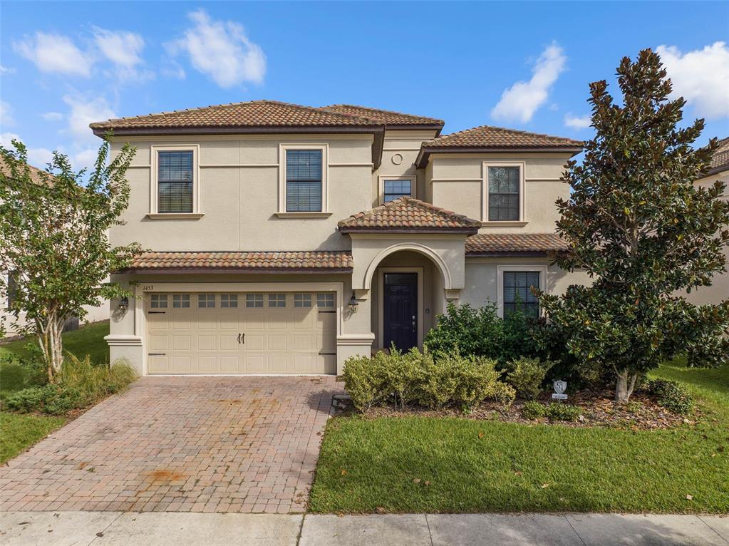 A two-story beige stucco house features a tile roof, arched entryway, and brick paver driveway — 1453 BELLE TERRE ROAD, DAVENPORT, FL