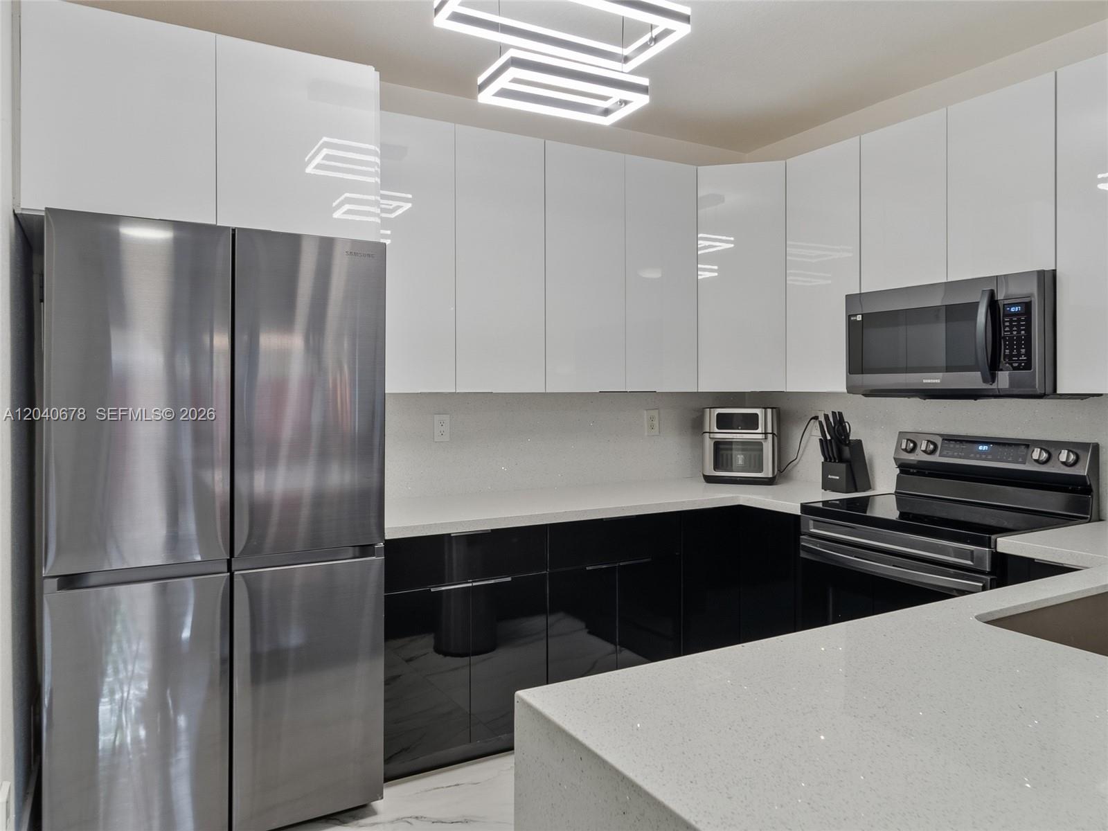 A modern kitchen features white upper cabinets, black lower cabinets, and stainless steel appliances — 1420 NE 33rd Ave # 15, Homestead FL 33033, HOMESTEAD, FL