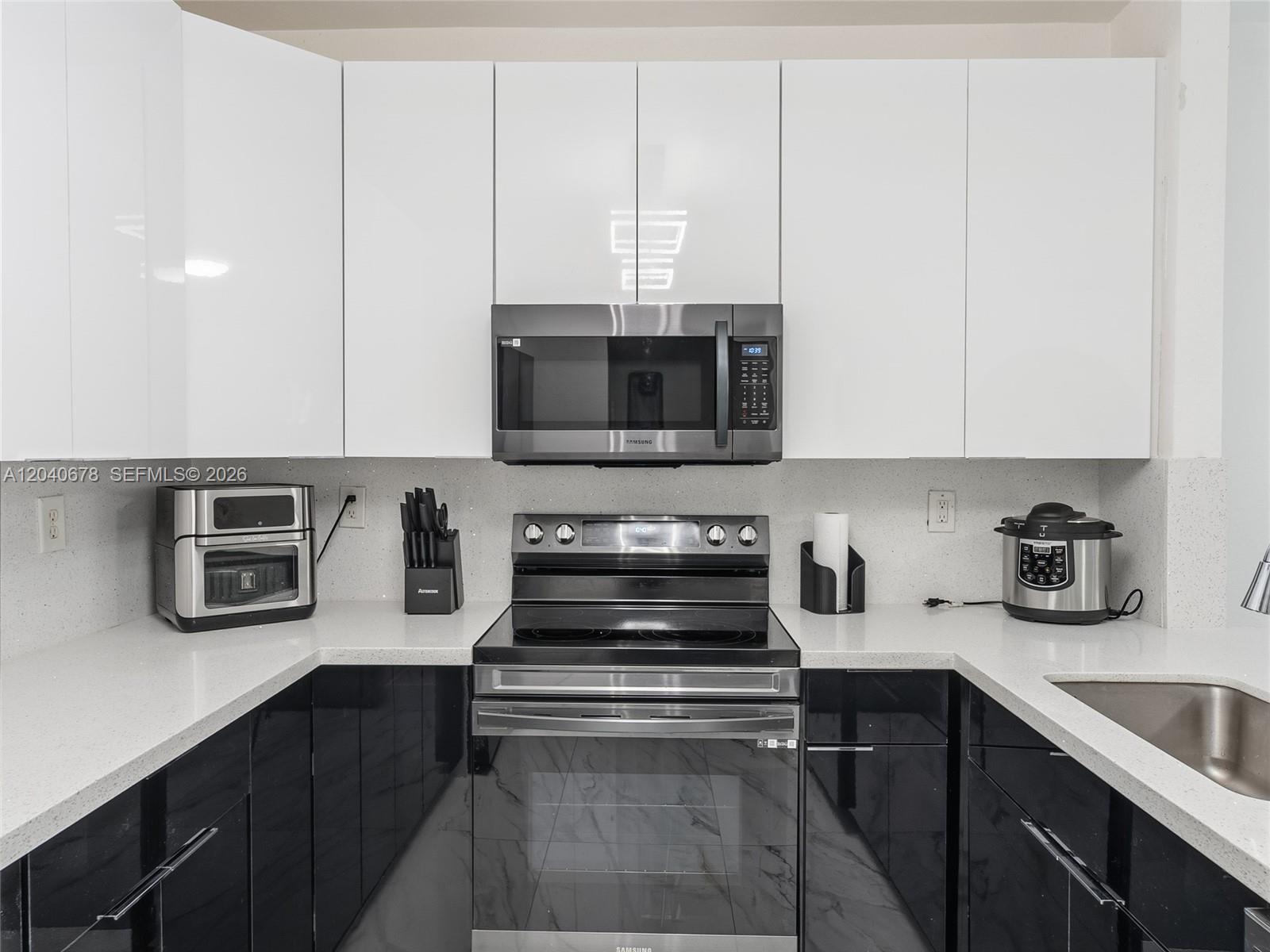 A modern kitchen features white upper cabinets, black lower cabinets, and a stainless steel stove — 1420 NE 33rd Ave # 15, Homestead FL 33033, HOMESTEAD, FL