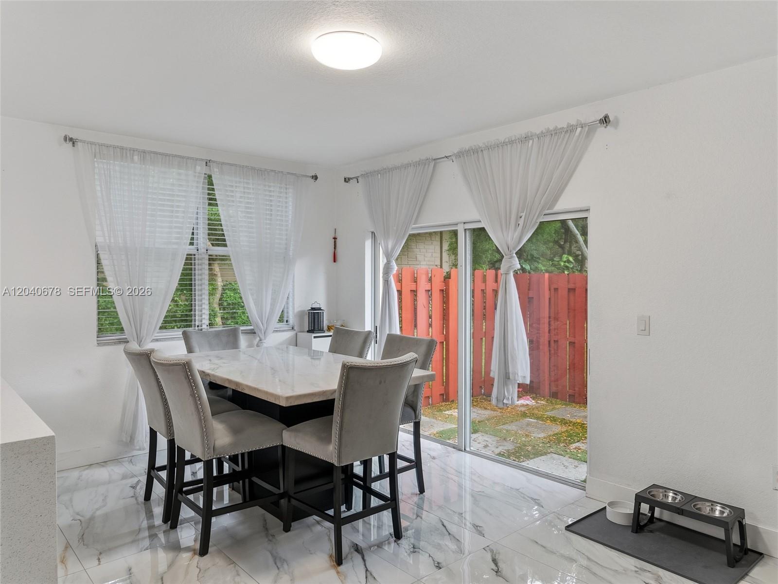 A dining room features a marble-topped table, upholstered chairs, tile flooring, and sliding glass doors — 1420 NE 33rd Ave # 15, Homestead FL 33033, HOMESTEAD, FL