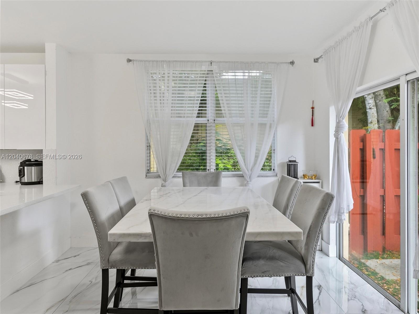 A dining area features a marble table, gray upholstered chairs, and a sliding glass door — 1420 NE 33rd Ave # 15, Homestead FL 33033, HOMESTEAD, FL
