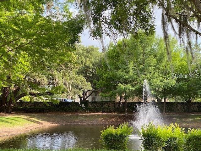 A fountain sprays water in a pond surrounded by trees and a stone wall — 2900 EDENSHIRE WAY UNIT 107, KISSIMMEE, FL