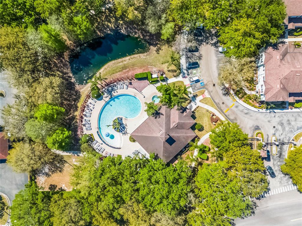 An aerial view shows a swimming pool, clubhouse, and small pond surrounded by trees — 2900 EDENSHIRE WAY UNIT 107, KISSIMMEE, FL