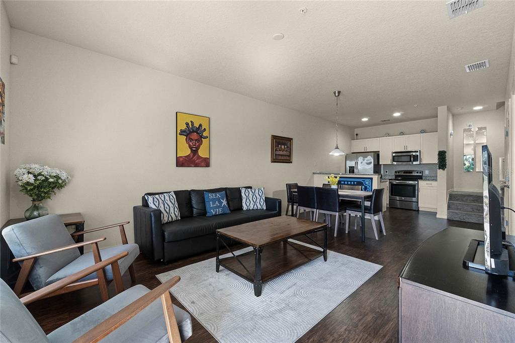 An open-concept living and dining area features dark wood flooring, a black sofa, and kitchen — 2900 EDENSHIRE WAY UNIT 107, KISSIMMEE, FL