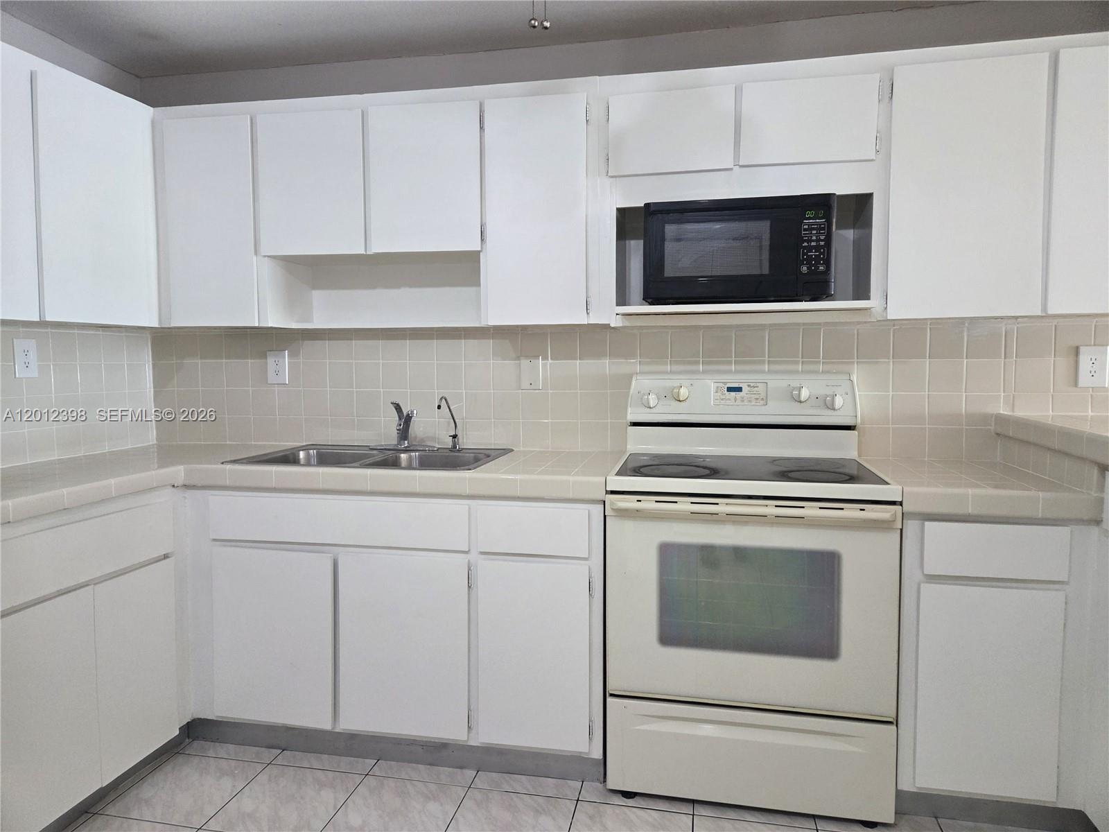 A kitchen features white cabinets, a black microwave, a white stove, and tiled countertops — 4670 W 13th Ln # 507, Hialeah FL 33012, HIALEAH, FL