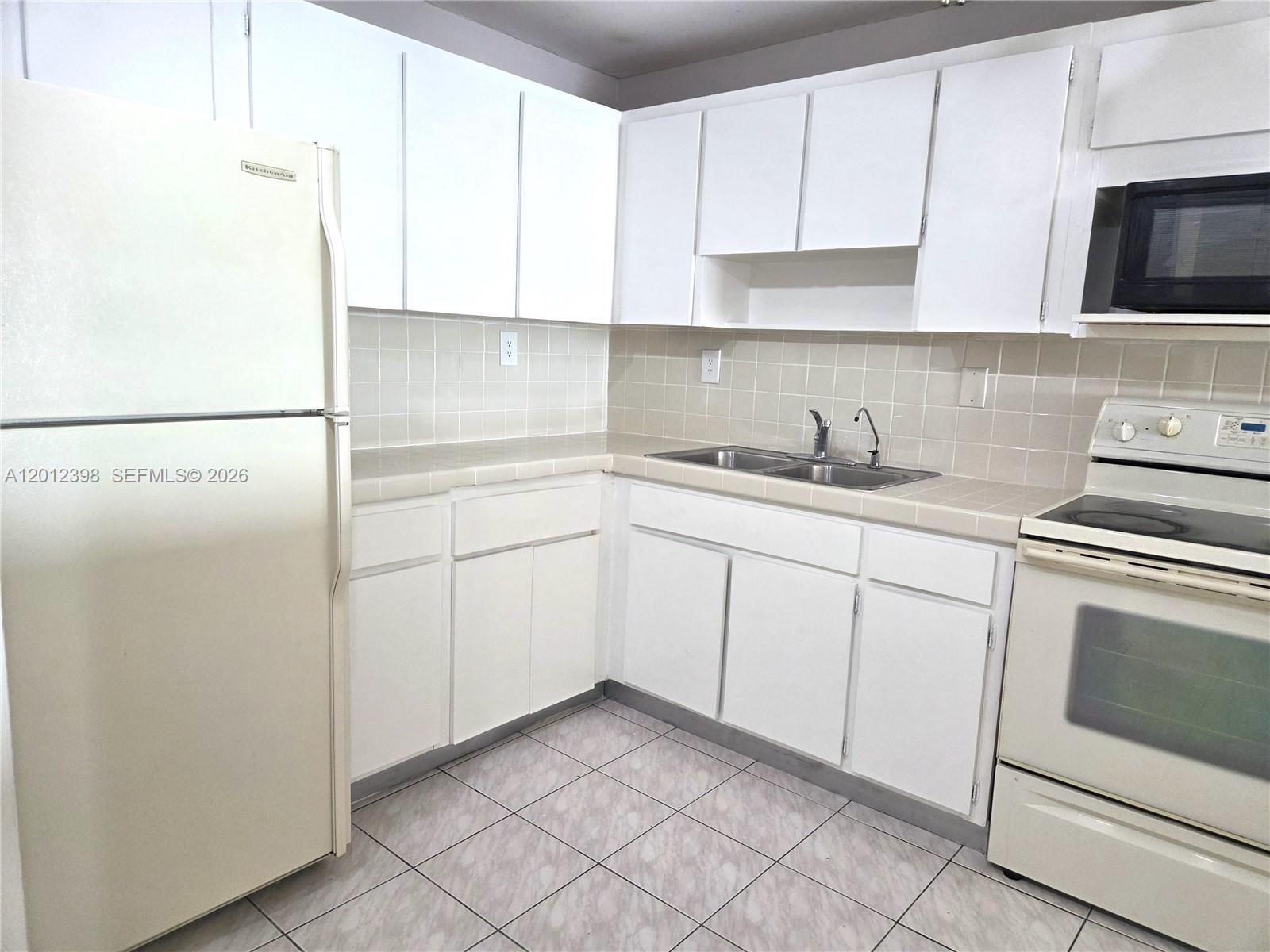 A kitchen features white cabinets, a double sink, tiled countertops, and white appliances — 4670 W 13th Ln # 507, Hialeah FL 33012, HIALEAH, FL