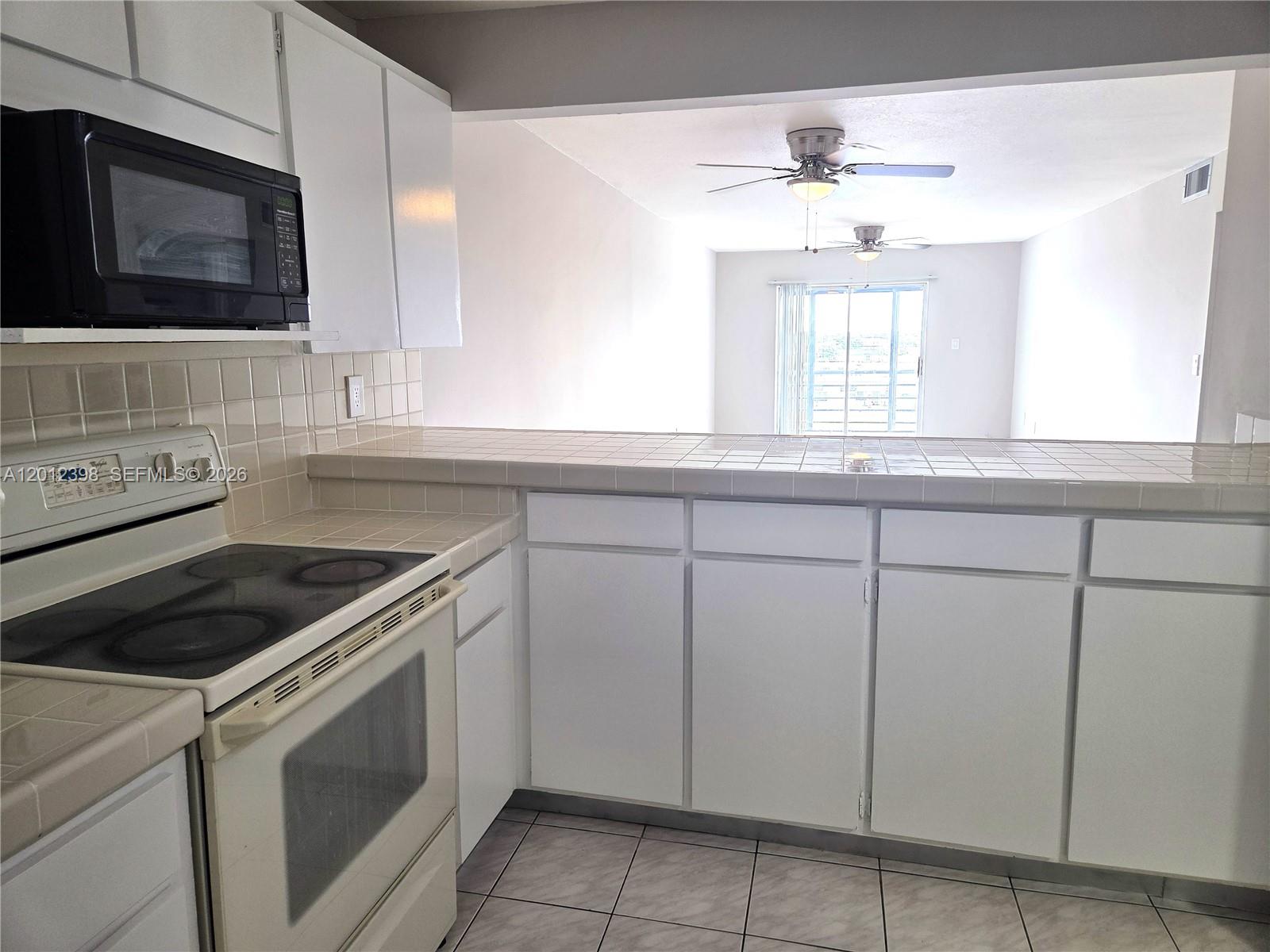 A kitchen with white cabinets, tiled countertops, and a stove overlooks an open living area — 4670 W 13th Ln # 507, Hialeah FL 33012, HIALEAH, FL