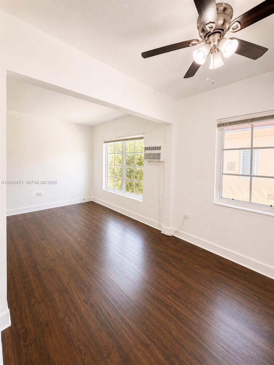 An empty room features dark wood-look flooring, white walls, a ceiling fan, and two windows — 322 25th St # 12, Miami Beach FL 33140, MIAMI BEACH, FL