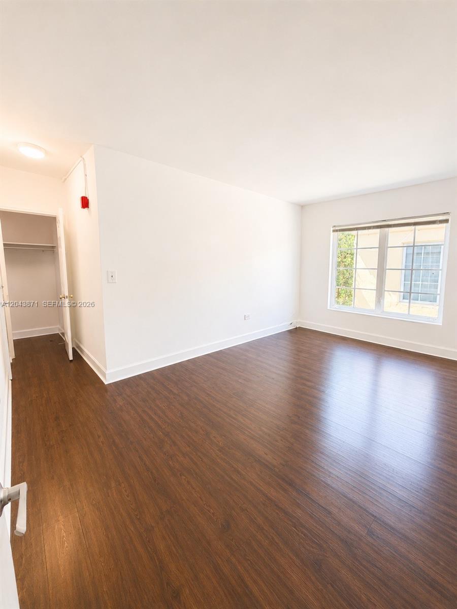 An empty bedroom features dark wood-look flooring, white walls, a window, and a closet — 322 25th St # 12, Miami Beach FL 33140, MIAMI BEACH, FL