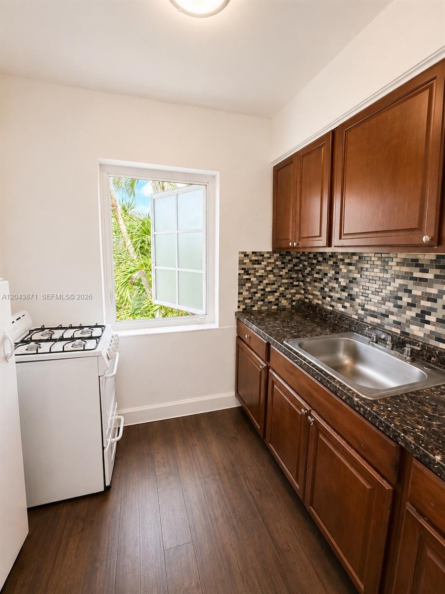 A small kitchen features dark wood cabinets, a mosaic tile backsplash, and a gas stove — 322 25th St # 12, Miami Beach FL 33140, MIAMI BEACH, FL