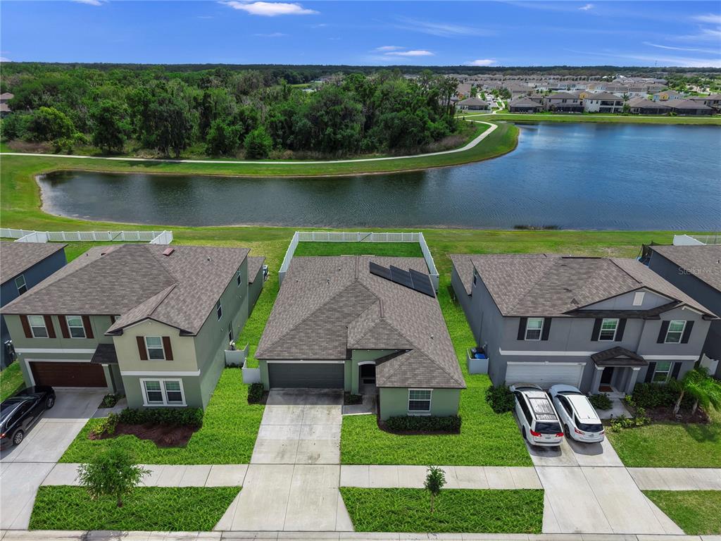 An aerial view shows three suburban houses with driveways facing a lake and trees — 12873 TRIPOLI AVENUE, RIVERVIEW, FL
