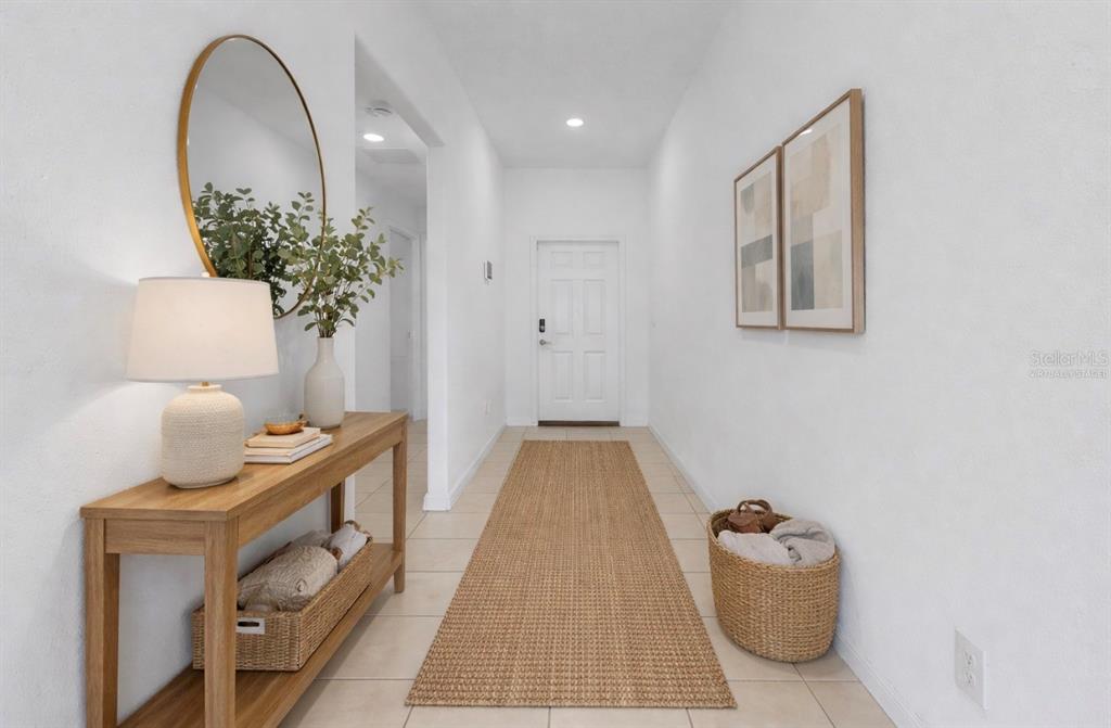 A bright entryway features a wooden console table, a round mirror, and a woven runner rug — 12873 TRIPOLI AVENUE, RIVERVIEW, FL
