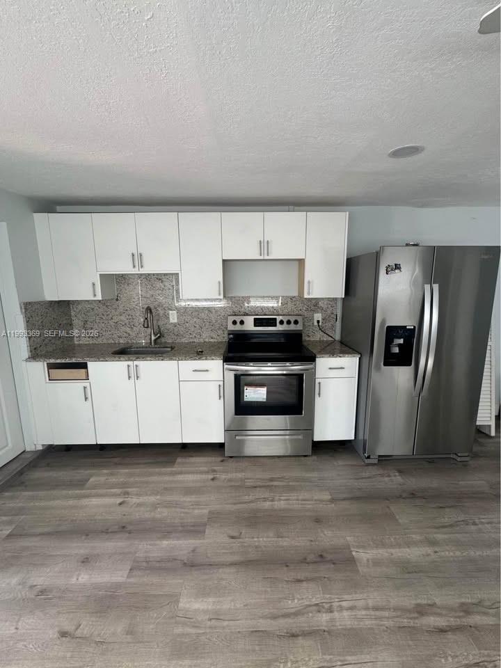 A kitchen features white cabinets, stainless steel appliances, granite countertops, and light wood-look flooring — 7620 SW 21 # 2, Miami FL 33155, MIAMI, FL