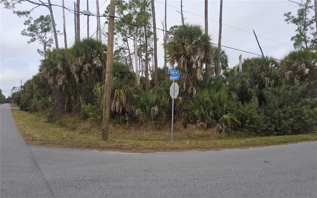 A street corner features a sign for Tulsa and Oklahoma streets beside a wooded lot — LOT 17 OKLAHOMA STREET, NORTH PORT, FL