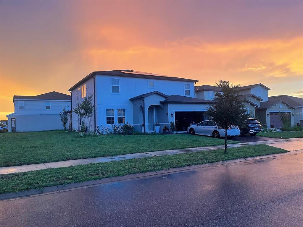A two-story suburban house with a garage and driveway under a vibrant sunset sky — 1100 LONE PALM WAY, ST CLOUD, FL