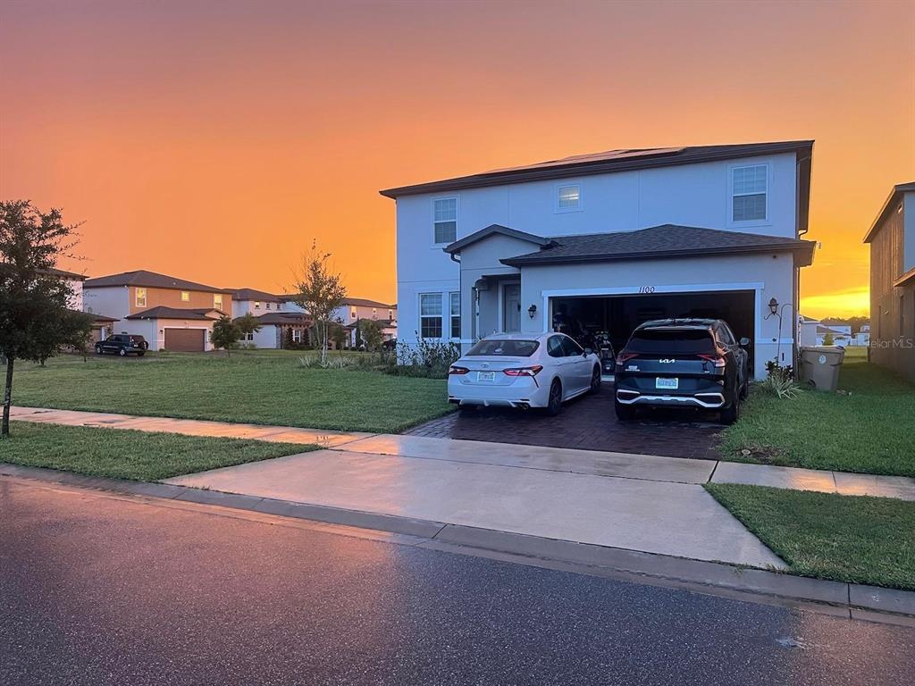 A two-story house with a two-car garage and two parked vehicles at sunset — 1100 LONE PALM WAY, ST CLOUD, FL