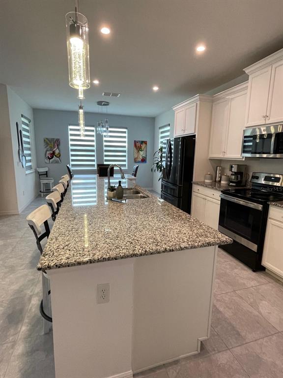 A kitchen features a large granite-topped island, white cabinetry, and stainless steel appliances — 1100 LONE PALM WAY, ST CLOUD, FL