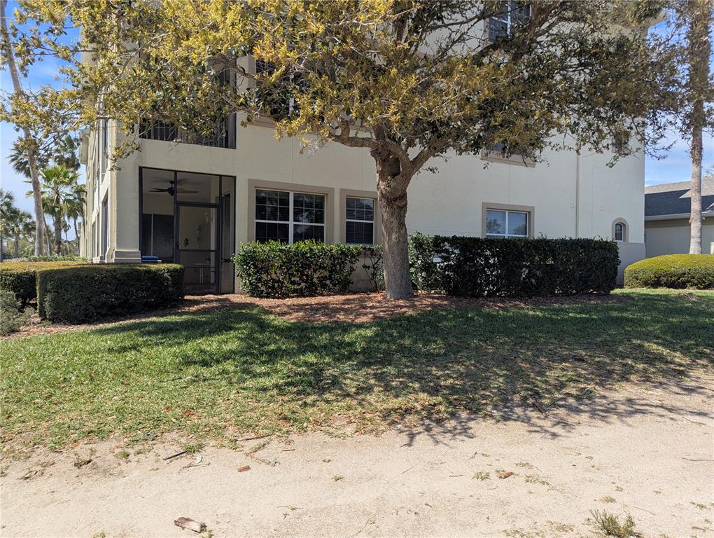 A multi-story building exterior features a screened-in porch, large windows, and mature landscaping — 200 RIVERFRONT DRIVE UNIT D101, PALM COAST, FL