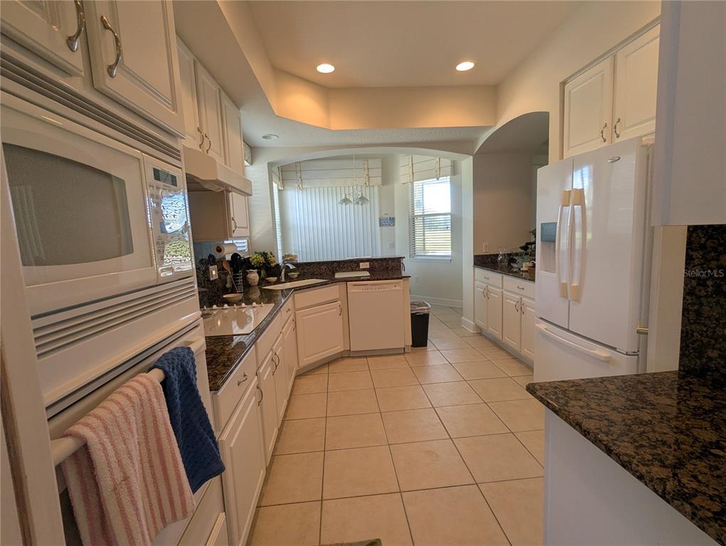 A kitchen features white cabinets, granite countertops, tile flooring, and stainless steel appliances — 200 RIVERFRONT DRIVE UNIT D101, PALM COAST, FL