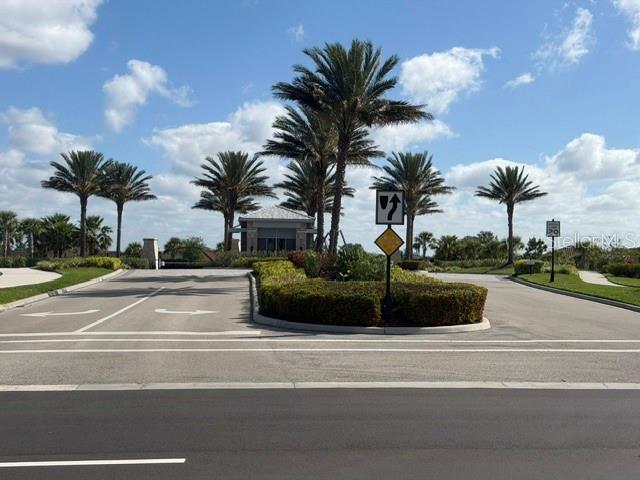 A paved road leads to a gated community entrance with palm trees and a guardhouse — 6289 MESA GLEN, BRADENTON, FL