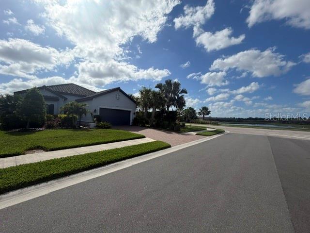 A single-story house with a garage sits next to a road and a lake — 6289 MESA GLEN, BRADENTON, FL