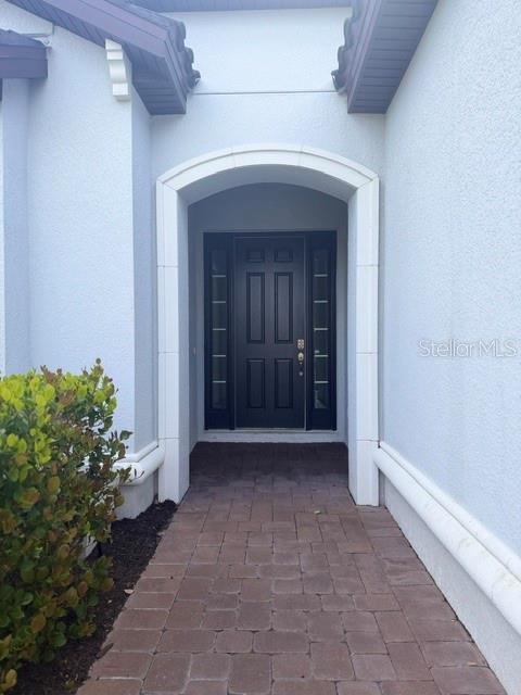 A dark front door with sidelights is framed by an arched entryway and brick walkway — 6289 MESA GLEN, BRADENTON, FL