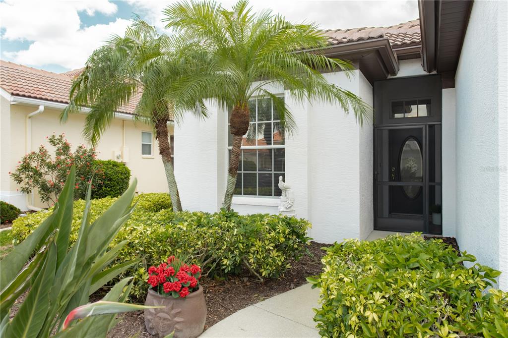 A white stucco house entrance features a screen door, a window, and two small palm trees — 624 SILK OAK DRIVE, VENICE, FL