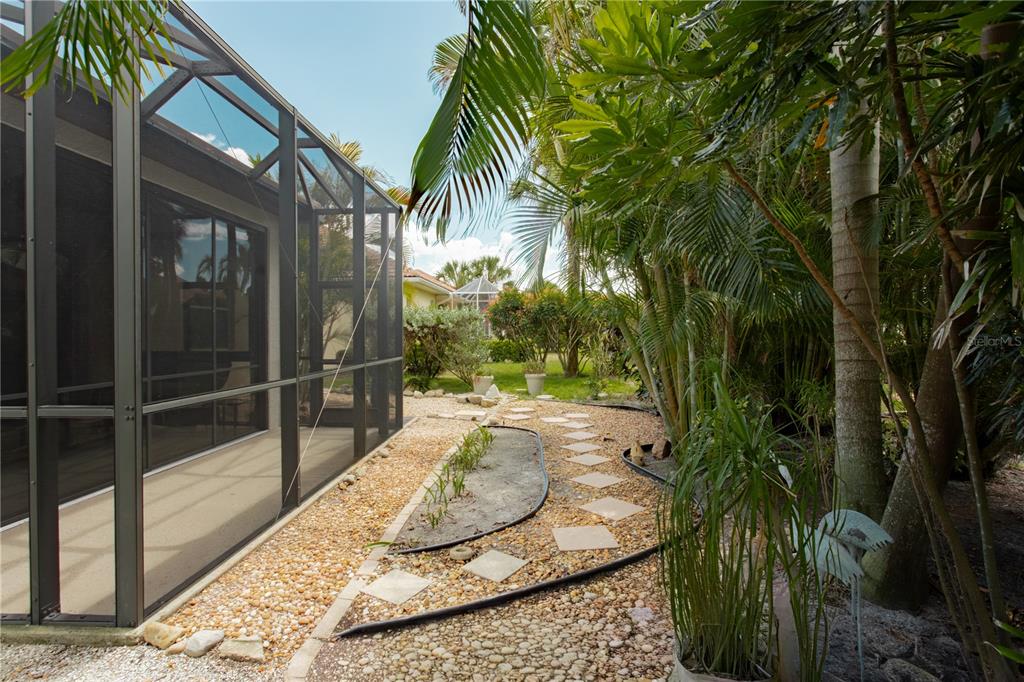 A stone path winds through a gravel yard beside a screened-in patio and palm trees — 624 SILK OAK DRIVE, VENICE, FL