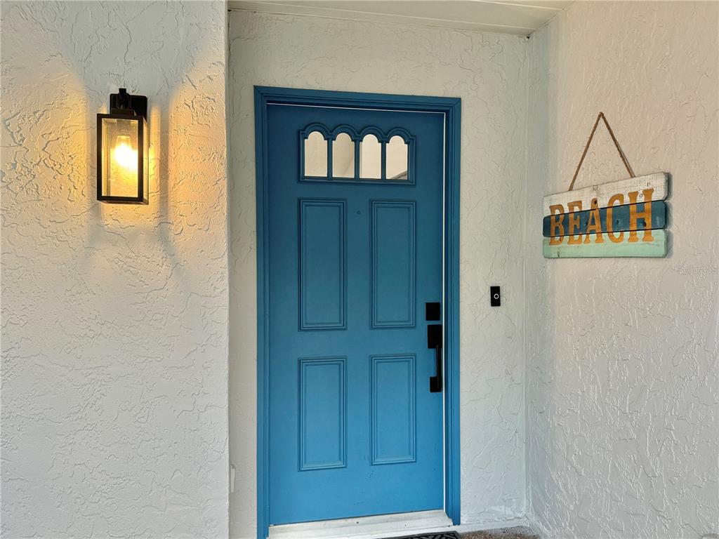 A bright blue front door with a small window sits beside a wall-mounted beach sign — 3409 45TH STREET W, BRADENTON, FL