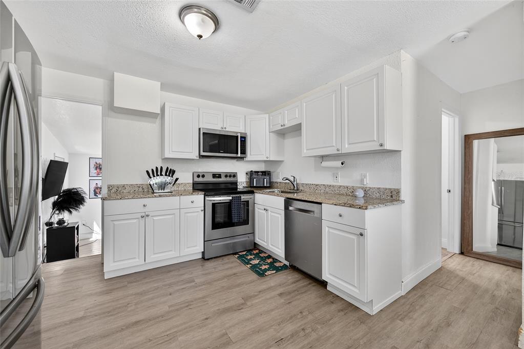 A kitchen with white cabinets, stainless steel appliances, and granite countertops on light wood flooring — 1318 SAN JOSE BOULEVARD, DAYTONA BEACH, FL