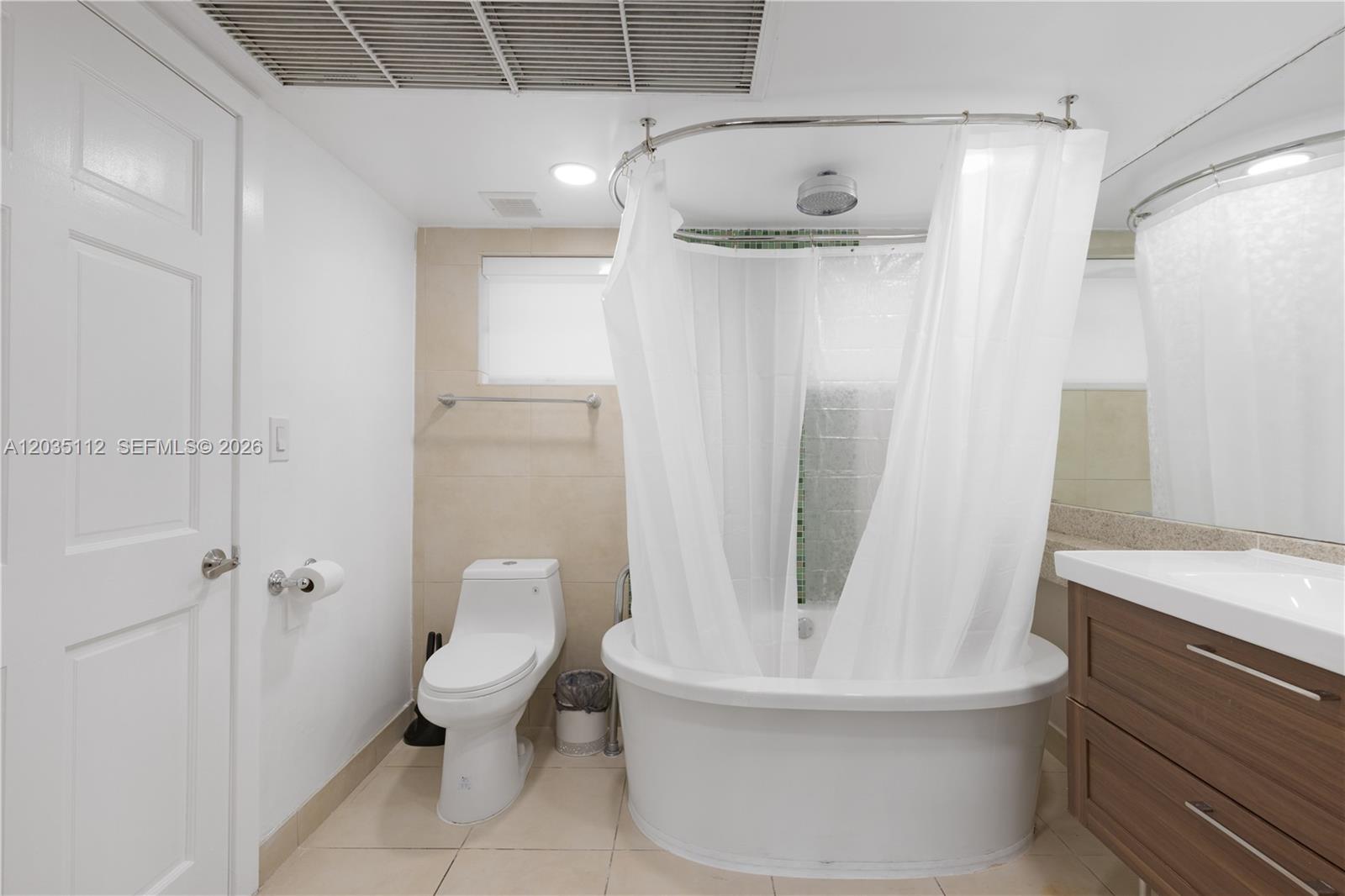 A bathroom features a white soaking tub, a toilet, and a wood-toned vanity — 1024 Ocean Dr # A402, Miami Beach FL 33139, MIAMI BEACH, FL