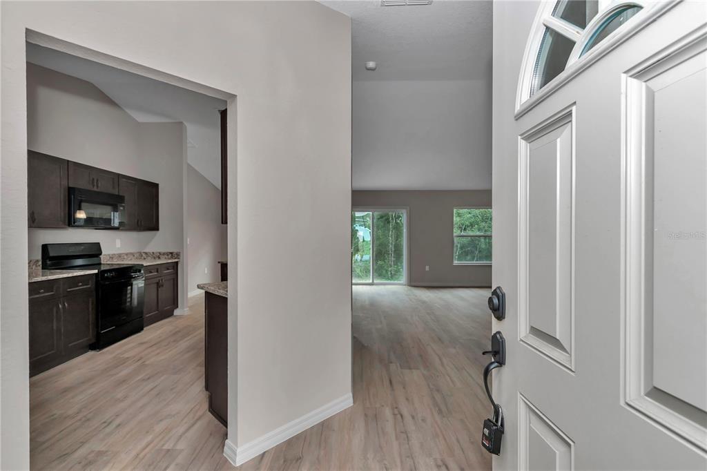 A view from an open front door into a kitchen and living area with wood-look flooring — 5780 NW 59TH COURT, OCALA, FL