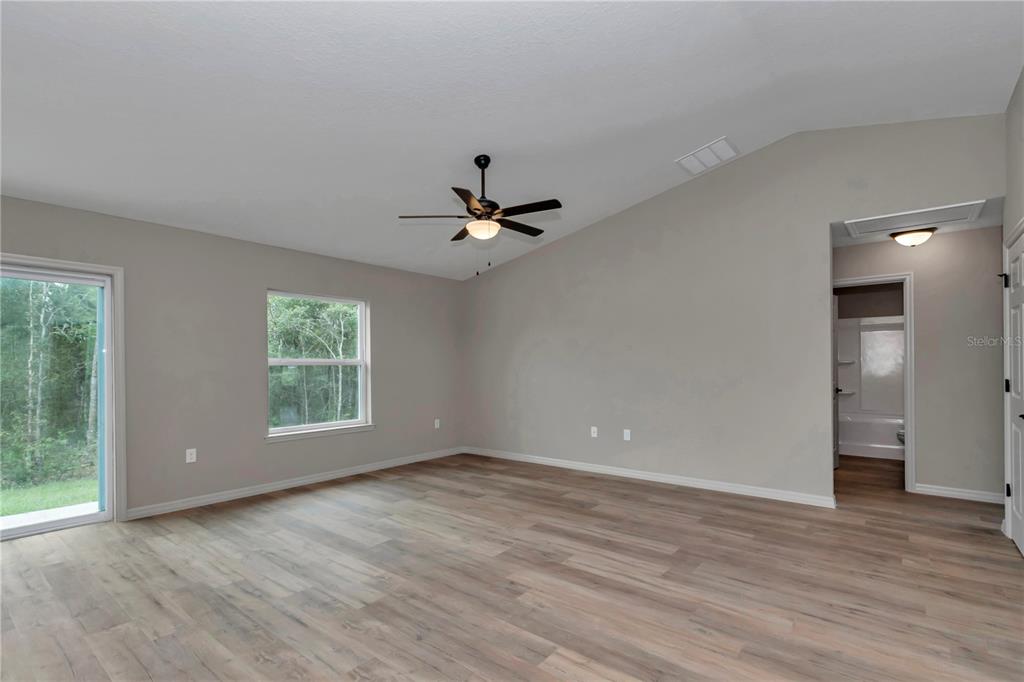 A spacious room with light gray walls, wood-look flooring, a ceiling fan, and sliding doors — 5780 NW 59TH COURT, OCALA, FL