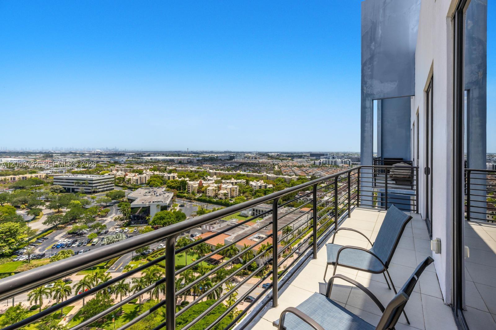 A high-rise balcony with two chairs overlooks a suburban landscape under a clear blue sky — 5350 NW 84th Ave # 2007, Doral FL 33166, DORAL, FL