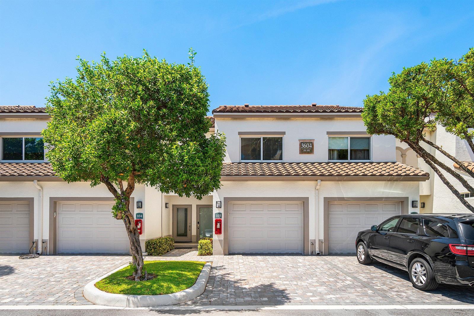 A two-story townhouse exterior features a paved driveway, two garage doors, and a small tree — 3604 S Ocean Boulevard # 105, Highland Beach FL 33487, HIGHLAND BEACH, FL