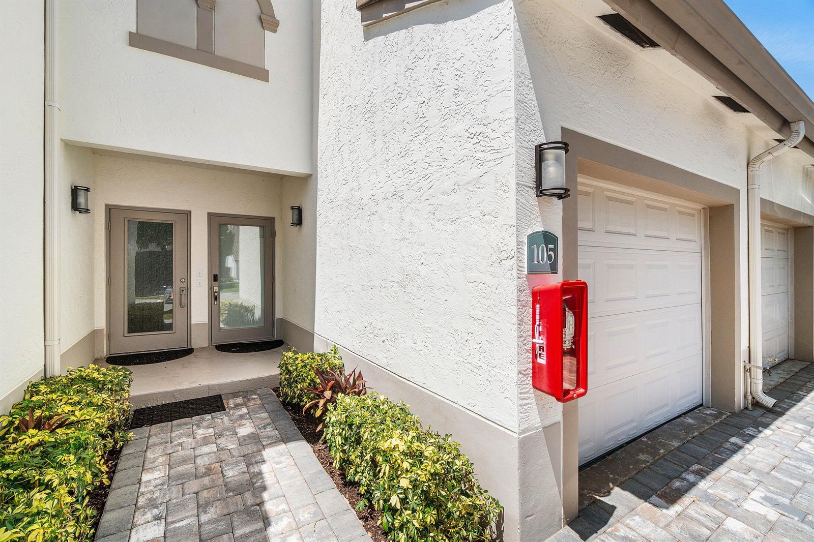 The exterior of a white stucco building features a front entrance, garage, and fire extinguisher — 3604 S Ocean Boulevard # 105, Highland Beach FL 33487, HIGHLAND BEACH, FL