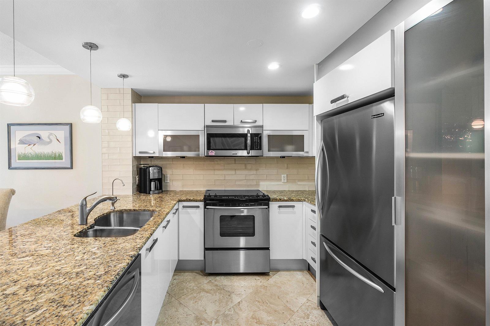 A kitchen features white cabinets, granite countertops, stainless steel appliances, and a tiled backsplash — 3604 S Ocean Boulevard # 105, Highland Beach FL 33487, HIGHLAND BEACH, FL